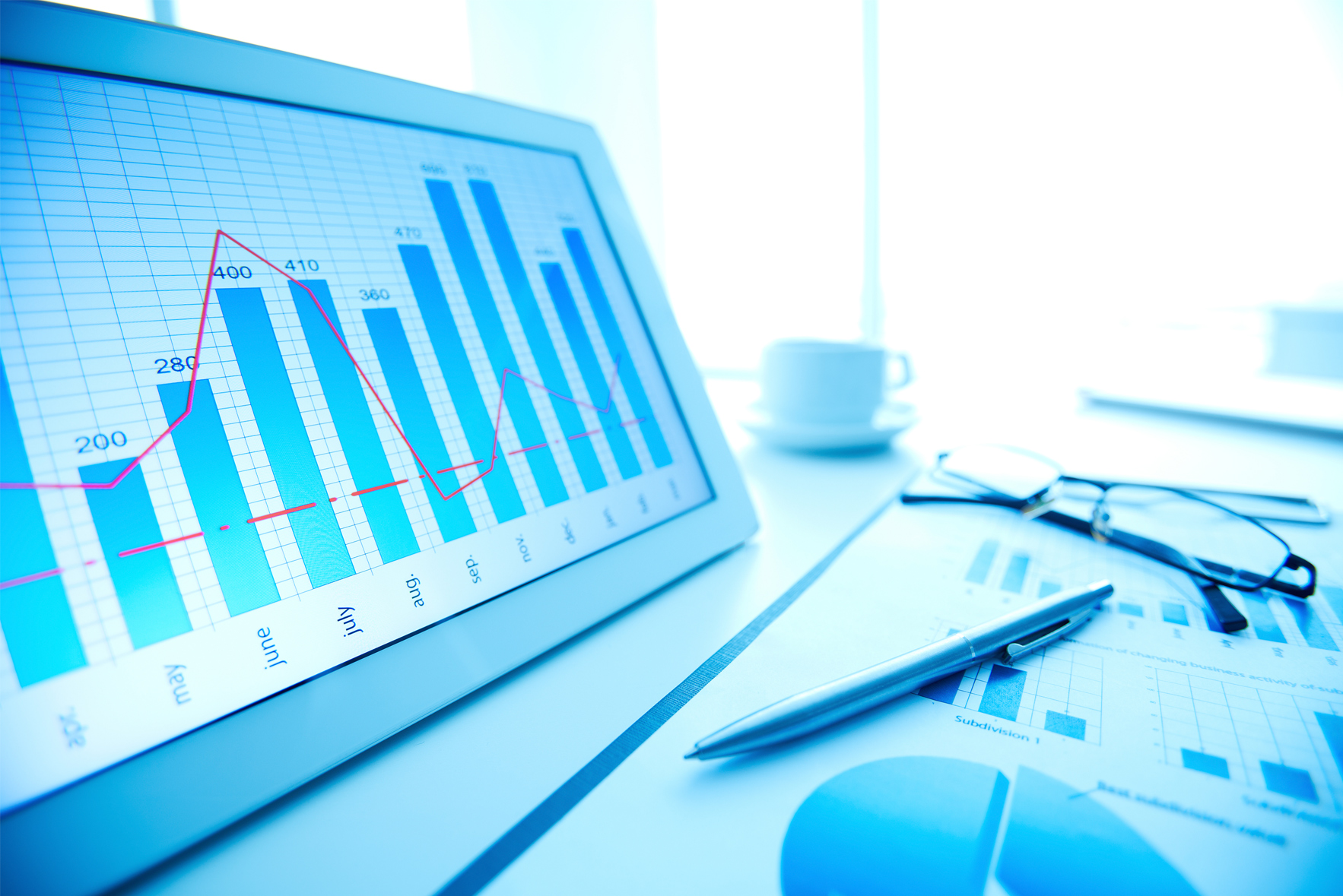 Uma empresária com um tablet e um notebook sobre alguns gráficos, ao centro, sobreposto, o nome Sírius ERP envolto de símbolos que remetem a eficiência, versatilidade e os retornos